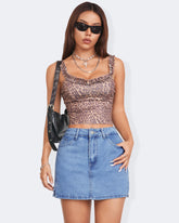 Model wearing a leopard print crop top and denim skort, showcasing trendy summer fashion with sunglasses and a black handbag.